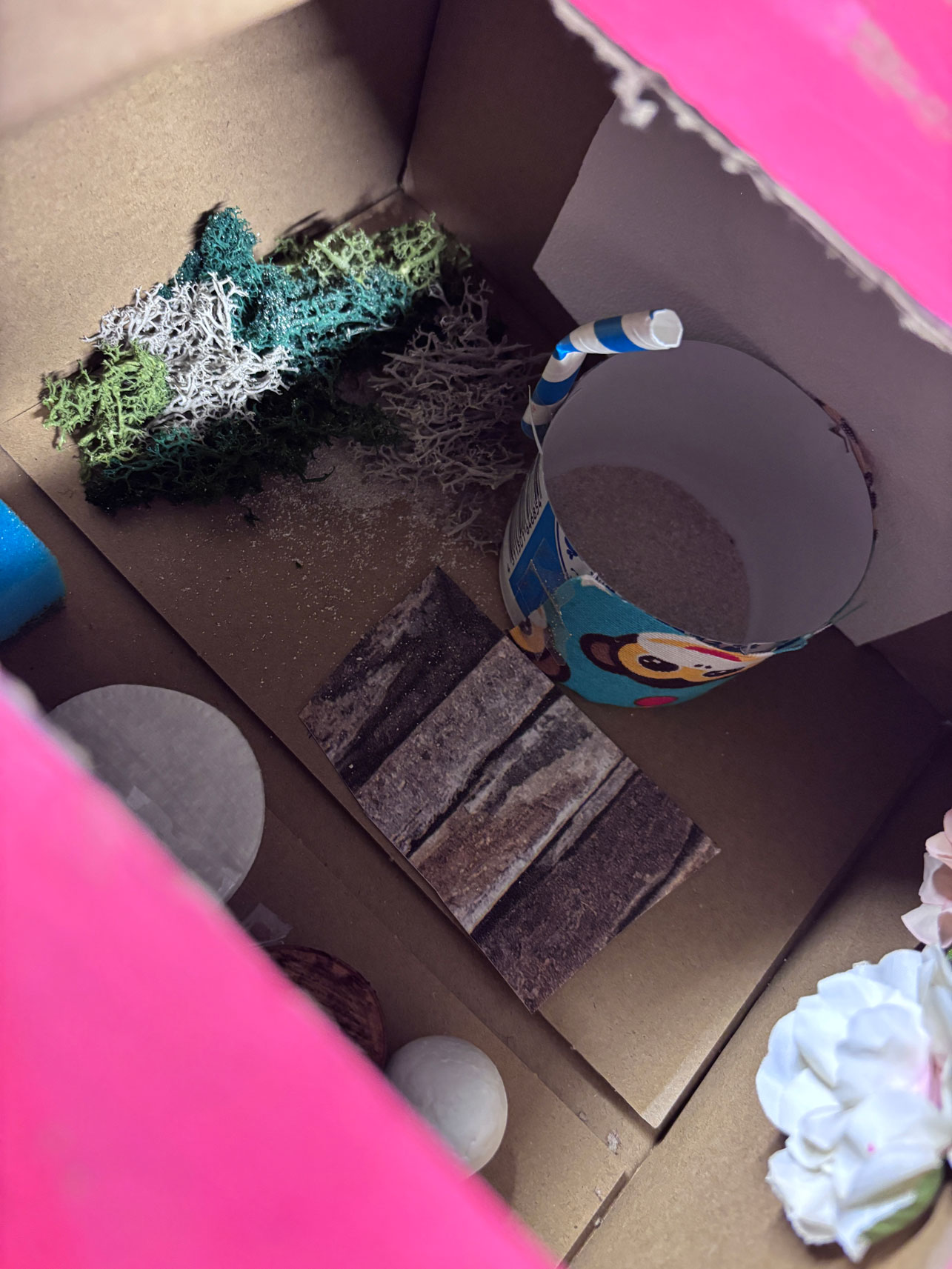Pappkiste mit Becher, Holz und Moos