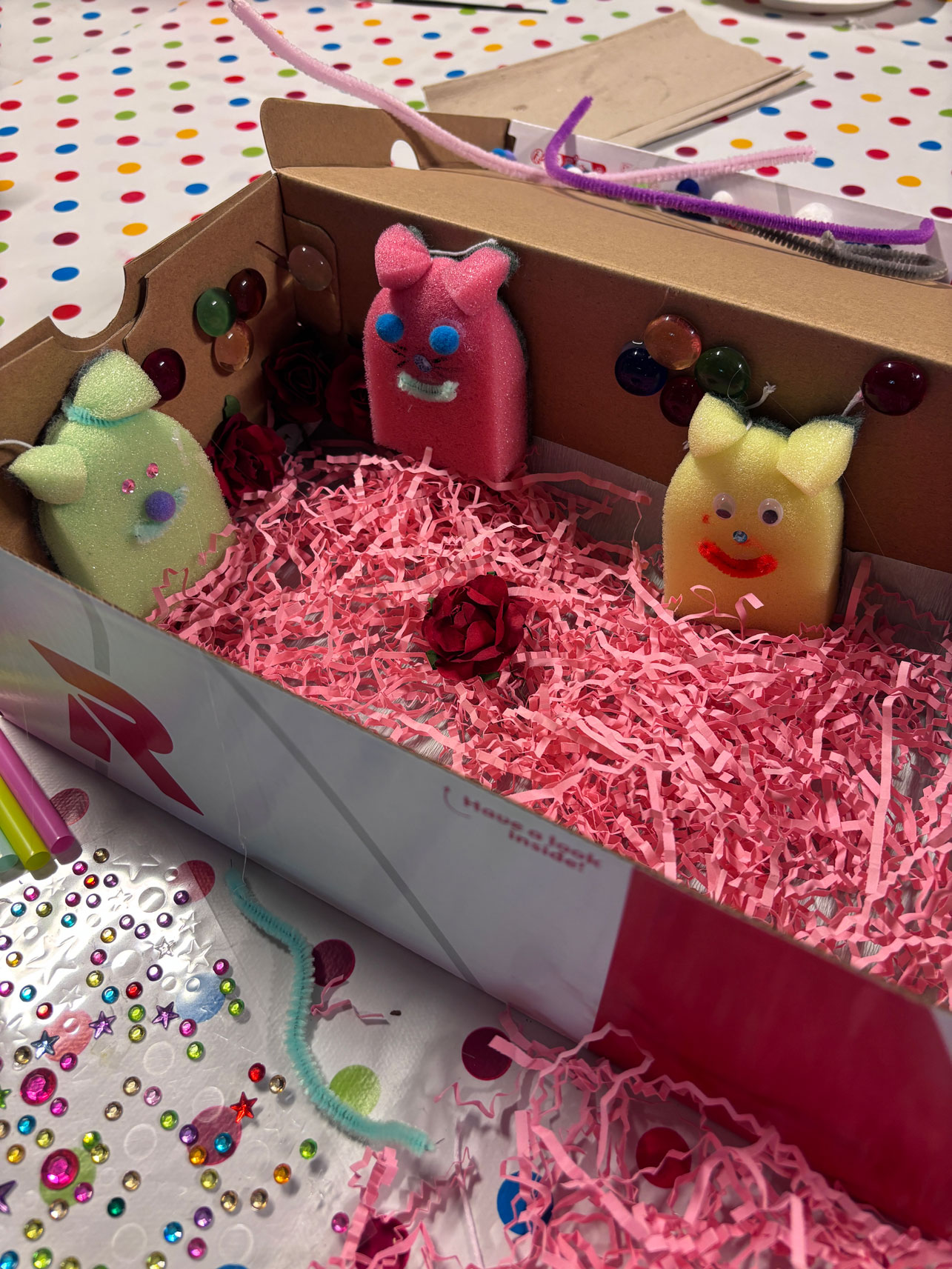 Pappbox mit rosa Papierschnipsen und Tierfiguren aus Topfschwämmen