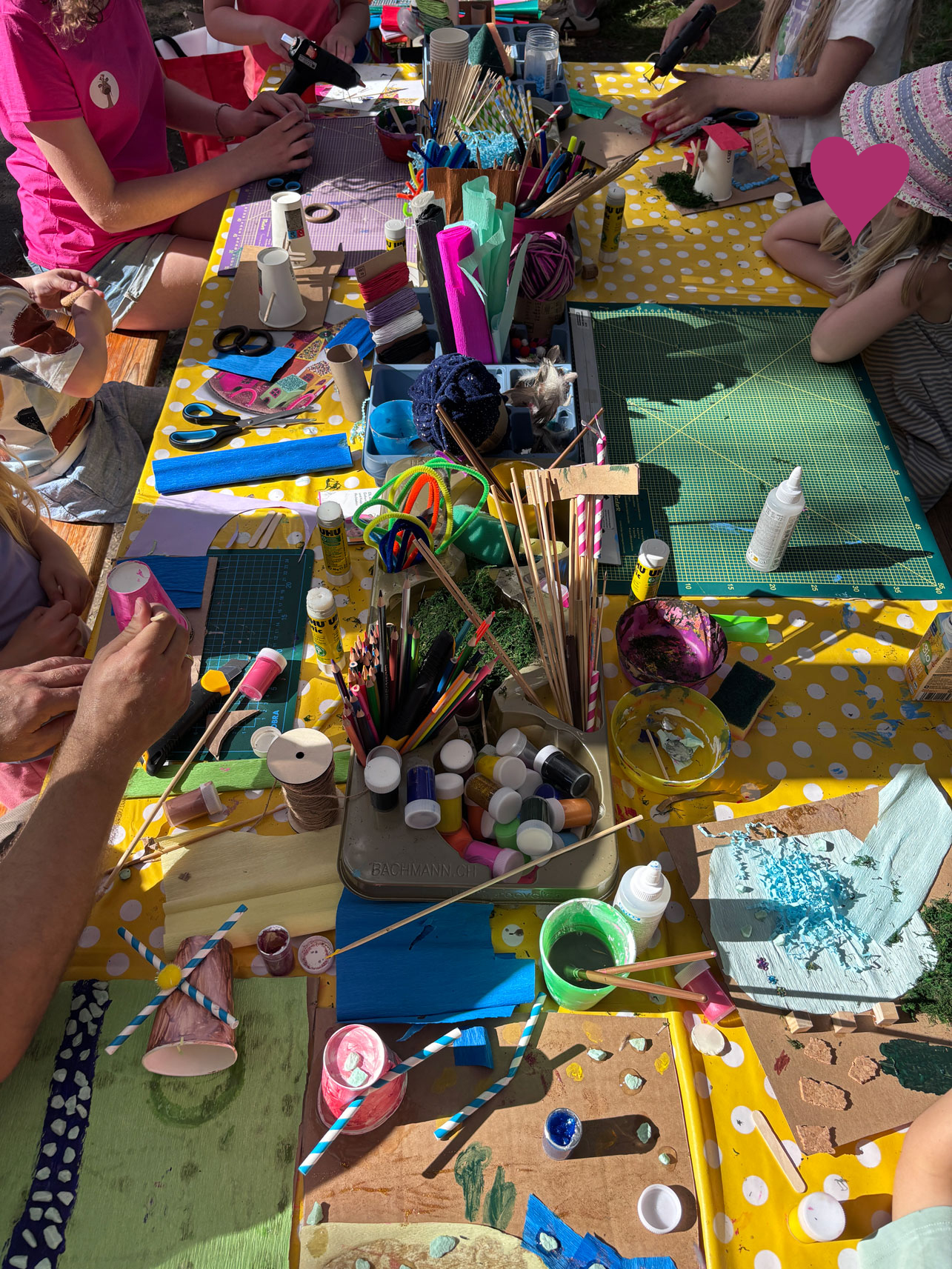 Kinder sitzen am Basteltisch mit vielen Materialien