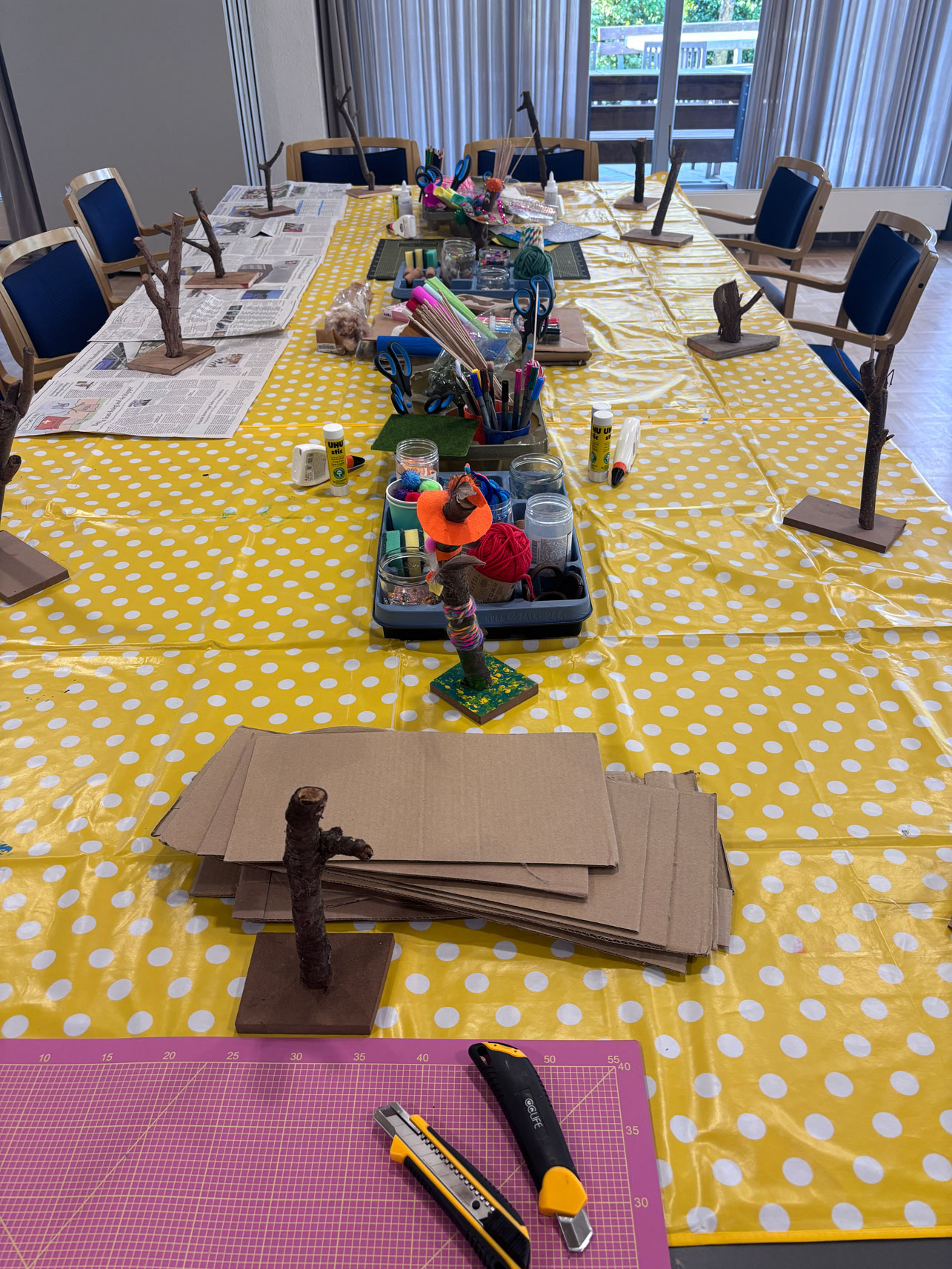 Blick in den Raum mit Arbeitstisch, gelb gepunkteter Tischdecke und Kreativmaterial in Kästen