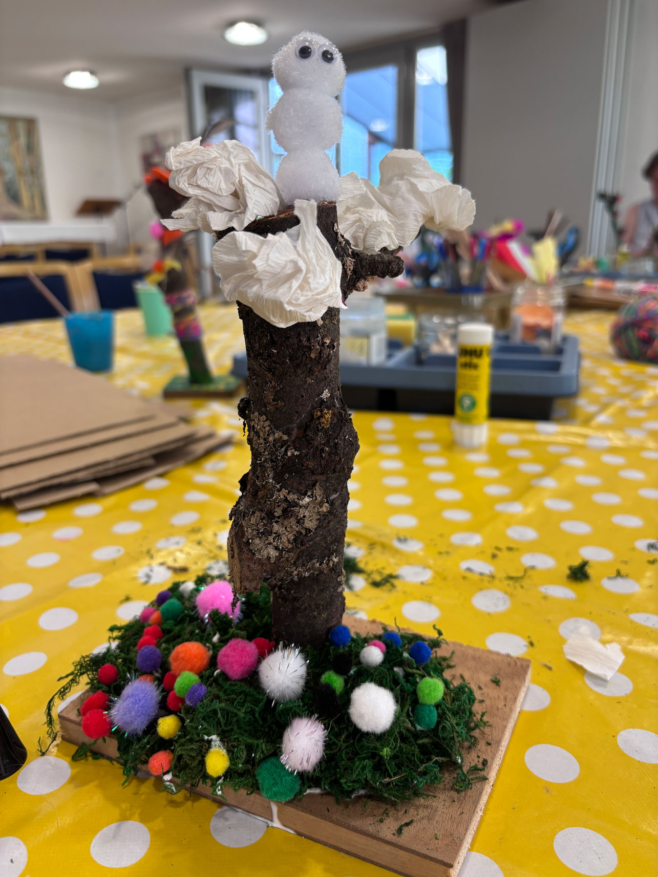 Baumhaus mit einem Schneemann aus Wattebäuschen obendrauf und Blumen an den Wurzeln